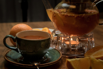 hot tea with sea buckthorn and orange near with a teapot and a candle