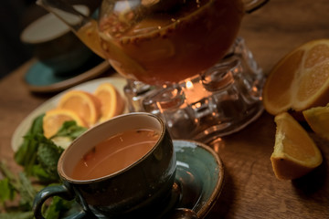 hot tea with sea buckthorn and orange near with a teapot and a candle