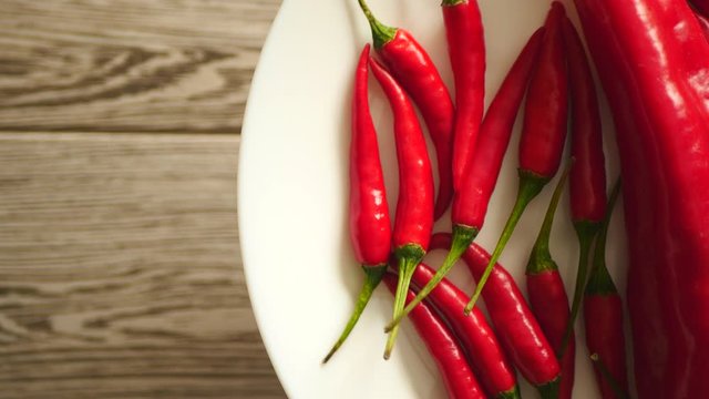 Top View Of Fresh Raw Red Chili Peppers And Ramiro Pepper Rotating On A White Plate On A Gray Wooden Background On The Right Side.