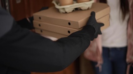 Man delivery pizza and coffe to customer in mask and gloves. Woman open door and take order. Coronavirus theme