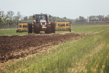 one blue tractor with a yellow trailer in a field unfolds before harrowing the ground