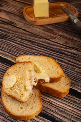 Fresh wheat toast with butter and a wooden butter dish with a piece of butter on a wooden background. Close up.