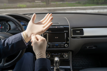 Middle age businessman in blue suit puts on rubber gloves for protect himself from bacteria and virus while driving a car. Coronavirus. Pandemic