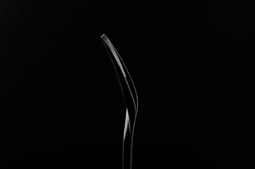 Black plastic fork on a black background. Contour light. Low key.