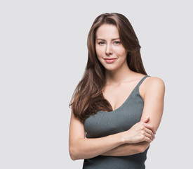 Obraz premium Beautiful young woman studio closeup portrait. Girl with crossed arms looking at camera isolated on gray background. Model with perfect clean skin. Beauty, makeup, healthy lifestyle, skin care concept