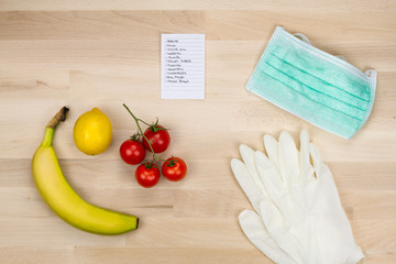 Grocery list with fresh fruits next to medical mask and latex gloves for personal protection while shopping. Shopping during pandemic.