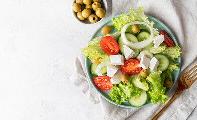 Greek salad with feta cheese, fresh vegetables and olives on white rustic background top view with copy space