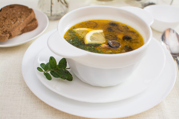 Traditional Russian meat soup solyanka with sausages, lemon and olives in a white ceramic bowl.