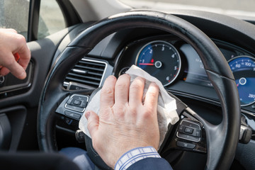 Middle age businessman in a blue suit cleaning steering wheel of a car using antivirus antibacterial wet wipe (napkin) for protect himself from bacteria and virus