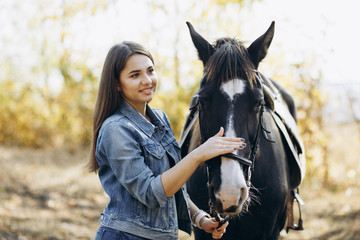 Obraz premium Beautiful stylish brunette woman near horse on ranch. Smiling girl hugging a horse. Human and animals relationship concept