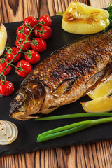 Grilled fish with vegetables, mushrooms and herbs on a black slate plate. Close up.