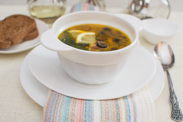 Traditional Russian meat soup solyanka with sausages, lemon and olives in a white ceramic bowl.