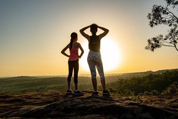 Two young women standing at the top of a mountain at sunrise.