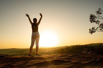 Fototapeta premium Young woman standing at the top of a mountain at sunrise.