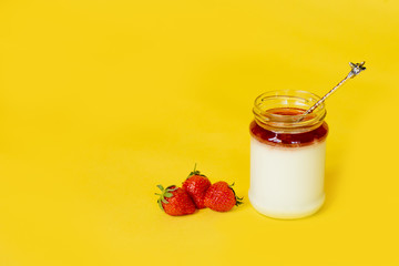 Red strawberry in glass jar and creamy white yogurt with jam on the yellow background