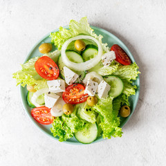 Greek salad with feta cheese, fresh vegetables and olives on white rustic background top view square orientation