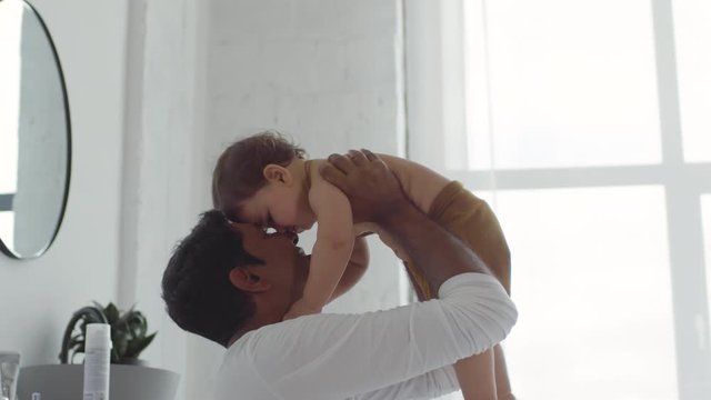 Medium shot of happy Indian father lifting adorable toddler girl and doing Eskimo kisses