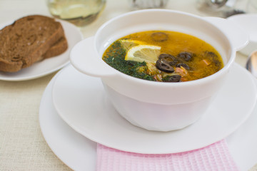 Traditional Russian meat soup solyanka with sausages, lemon and olives in a white ceramic bowl.