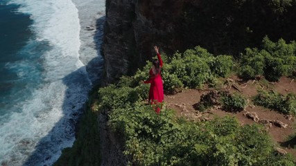 Aerial drone view of happy fit hipster young woman in red dress dance on the cliff mountain. Girl having fun enjoying nature celebrating vacation travel adventure. Adventure lifestyle travel concept. 