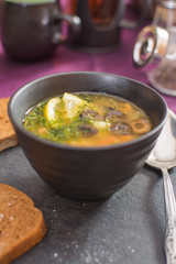 Traditional Russian meat soup solyanka with sausages, lemon and olives in a black ceramic bowl on a black stand made of natural stone.