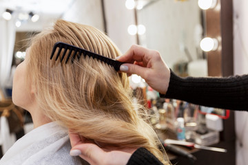 Fototapeta premium A blonde woman is combing her hair in a professional beauty salon. Beauty and care. Close-up. Back view.