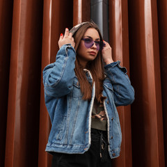 Fashionable beautiful young hipster woman puts on a hood. Attractive girl model in stylish denim...