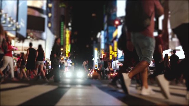 Cinematic slow motion side view of many people's legs crossing a busy city street at night on Times Square, New York.