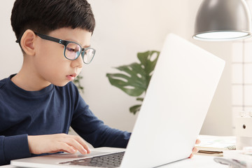 Online learning & Social distancing, Cute and adorable Asian little boy use computer laptop to study online lessons at home due to Covid-19 pandemic, city lockdown and school break