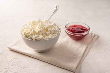Cottage cheese in a bowl with a spoon and fruit jam on a linen napkin on a light background