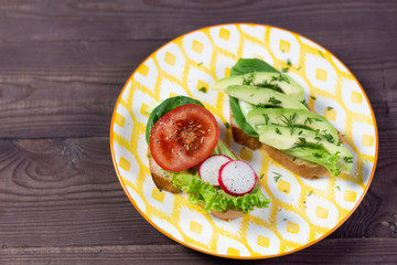 Open sandwiches with vegetables on colorful plate on wooden table