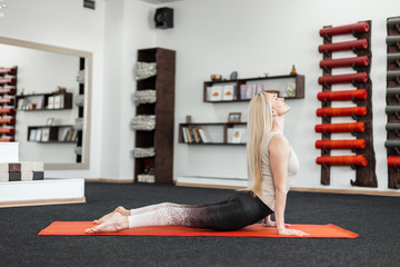 Professional young woman doing exercises for the back in fitness room on the mat. Girl does...