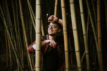 Fototapeta na wymiar A young guy in glasses with a beautiful smile enjoys in a bamboo forest