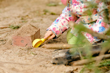 Close-up of mid section of a 4 year old caucasian girl in warm clothing playing outdoors with sand,...