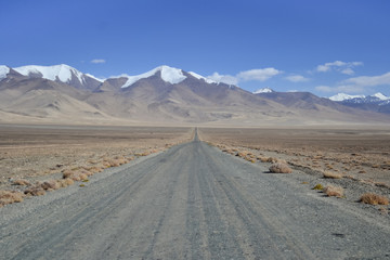 Fototapeta na wymiar Scenery gravel road with snow peaks mountains in the background