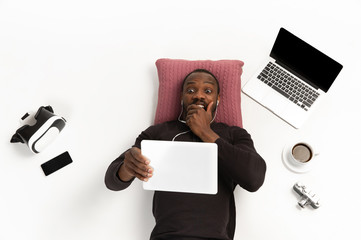 Young african-american man using devices, gadgets isolated on white studio background. Concept of...