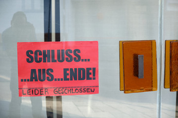 A red sign on the glass doors of a closed department store says "Schluss.... Aus.... Ende! Leider geschlossen" and informing about the closing down. Seen in Germany in June.