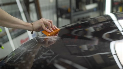 professional applying protective film to the red car. Master glues a protective film on the hood of...