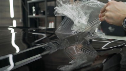 professional applying protective film to the red car. Master glues a protective film on the hood of...