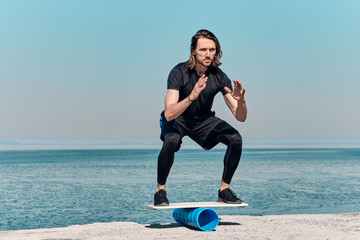 Closeup Of Healthy Handsome Active Man With Fit Muscular Body keeping balance on the wooden board against the background of sea on summer day