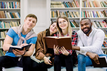 Four multiethnic cheerful students friends in the library, reading books, communicating and spend time together. Happy international book day