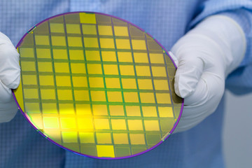 Hands in white gloves and blue suit holding a silicon wafer with microc hips on white background.