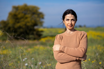 ragazza con maglione colo cachi guarda seria , sullo sfondo campagna e un prato naturale verde e...