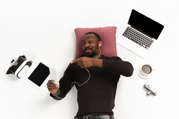 Young african-american man using devices, gadgets isolated on white studio background. Concept of...