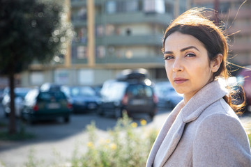 ragazza mora con la coda guarda seria , sullo sfondo palazzi e auto parcheggiate