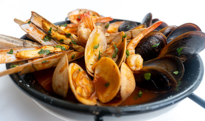 Sauteed shellfish and seafood in a black pan on a white background 