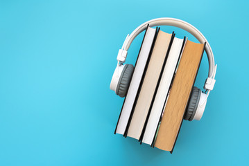 White headphones with stack of books on blue background. Audio books or modern education concept