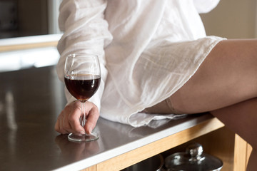 beautiful woman dressed in a man's shirt is drinking wine in the kitchen