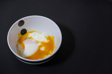 Soft-boiled eggs break when poured into a small white cup.Black background and copy space