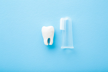 White tooth and transparent silicone fingertip toothbrush on light blue table background. Pastel color. Babies teeth hygiene. Closeup. Top down view.