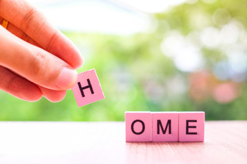 Hand holding H word is connect for home word written on pink color wood block on wooden and nature background, COVID-19 concept.